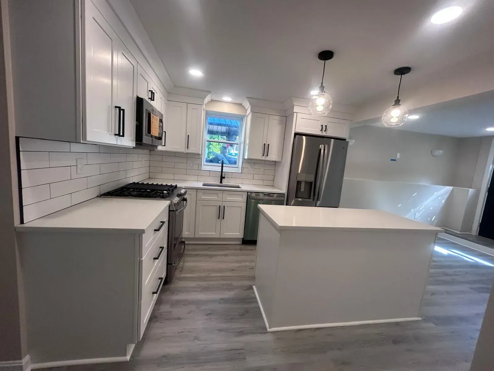Bright white kitchen with countertops, cabinets, and island. Stainless steel appliances, gray flooring, and pendant lights.