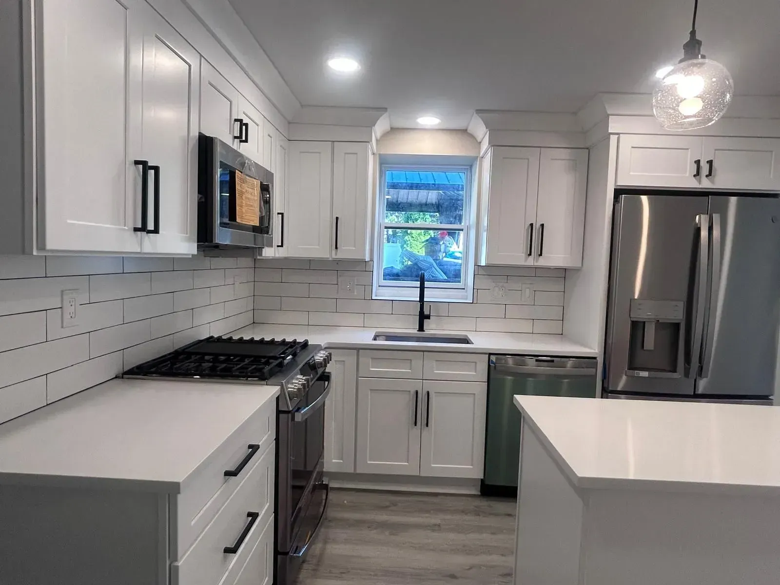White kitchen with stainless steel appliances, black hardware, and light-colored countertops.