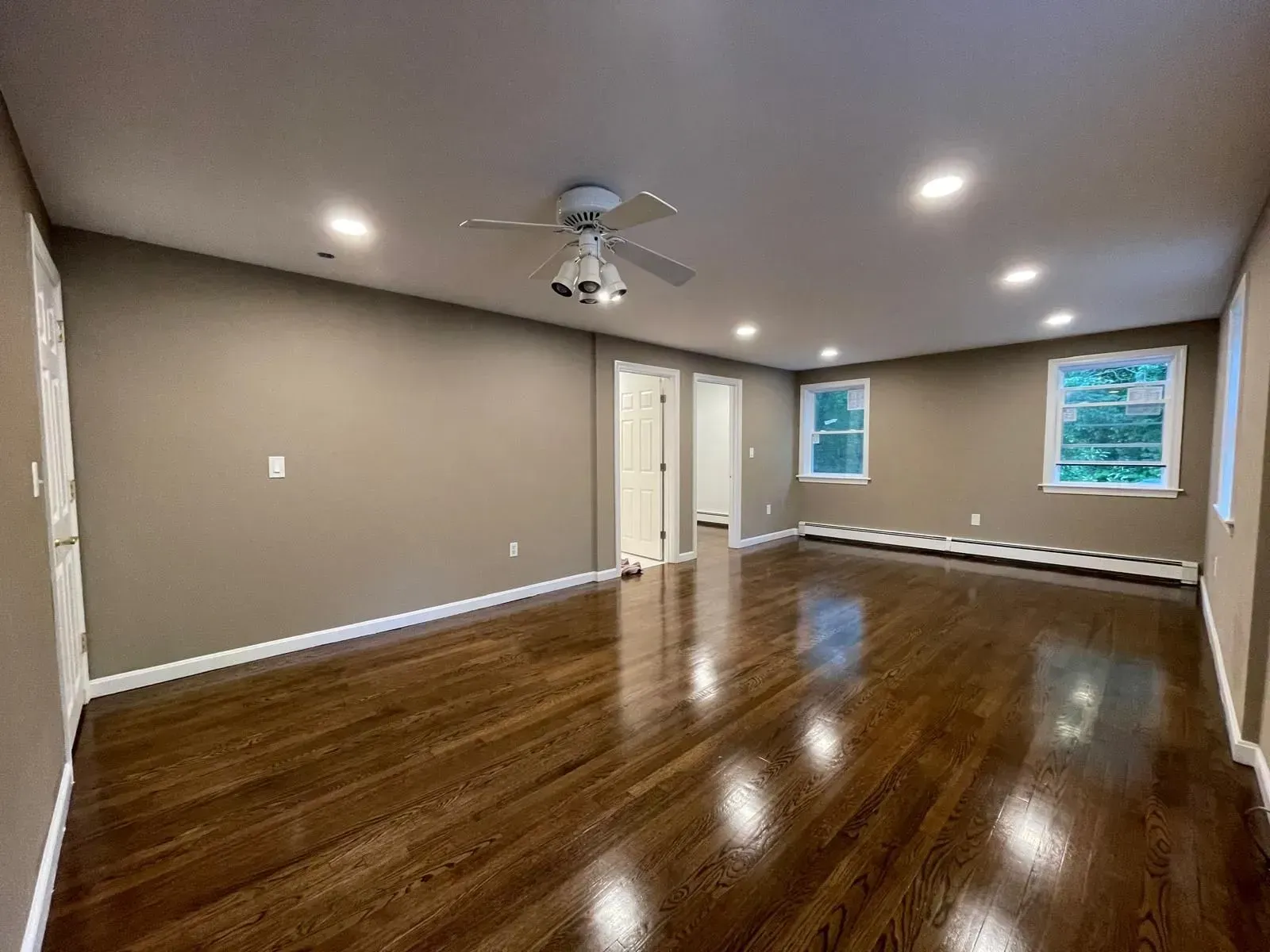 Empty room with dark wood floors, tan walls, ceiling fan, recessed lights, and white trim.