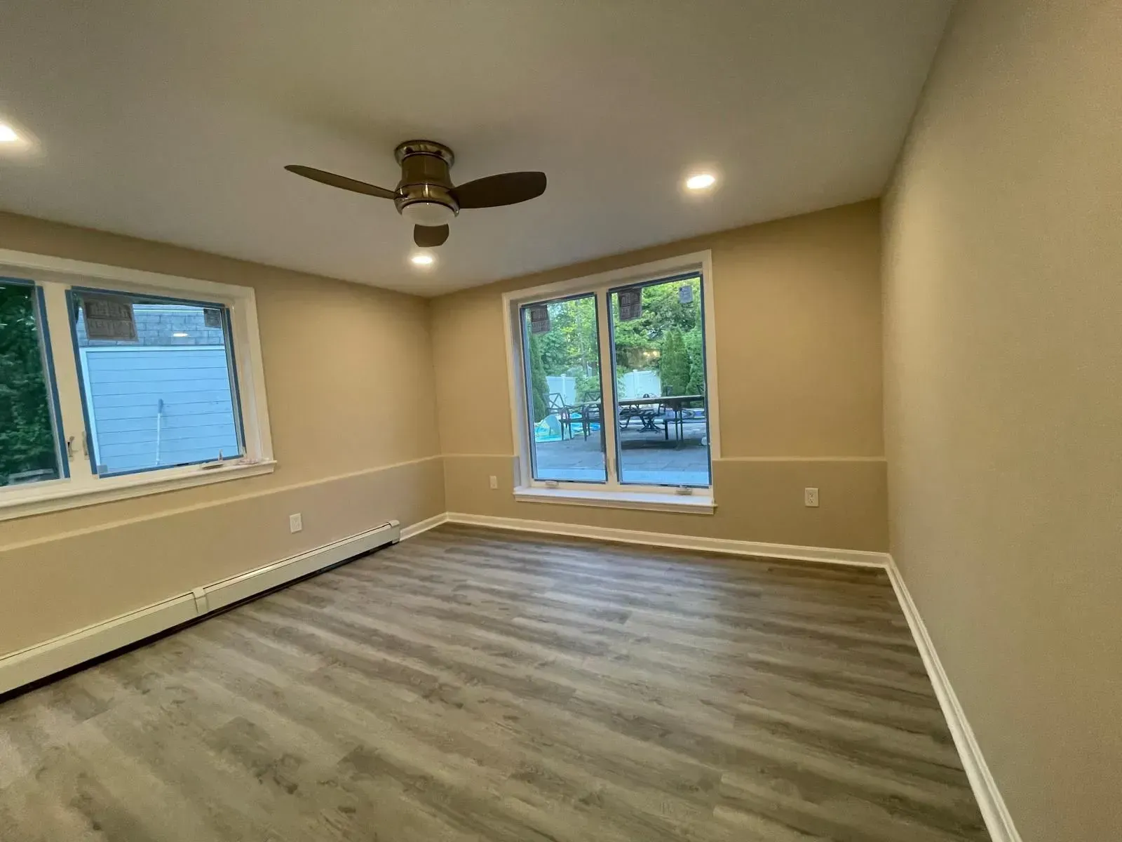 Empty room with gray wood-look flooring, beige walls, windows, and a ceiling fan.