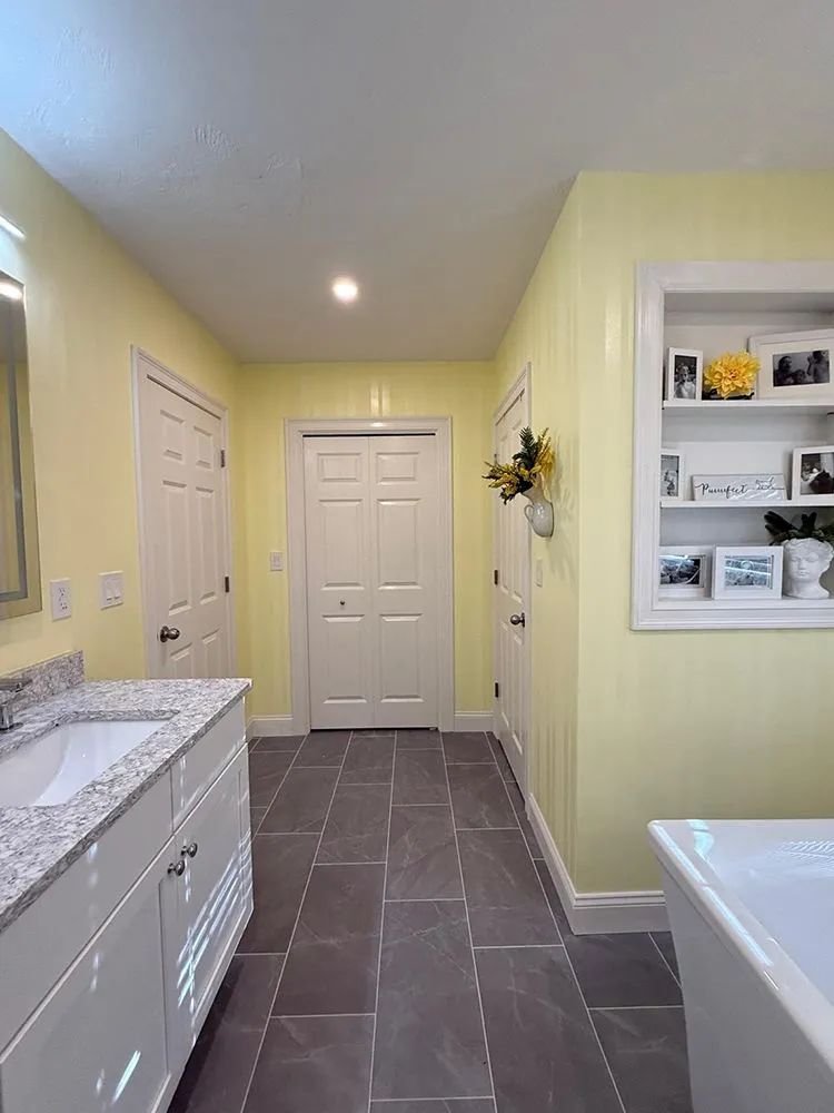 Bathroom with pale yellow walls, white vanity, and gray tiled floor. Built-in shelves with decor.