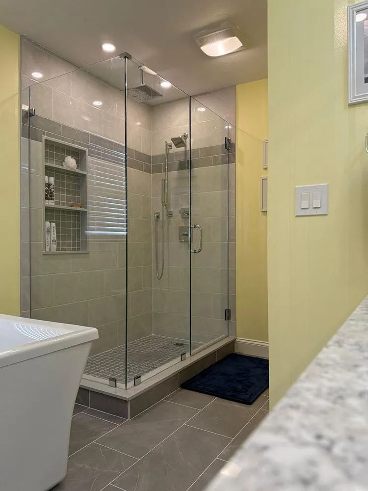 Modern bathroom with glass shower, gray tiles, yellow walls, and a white tub.