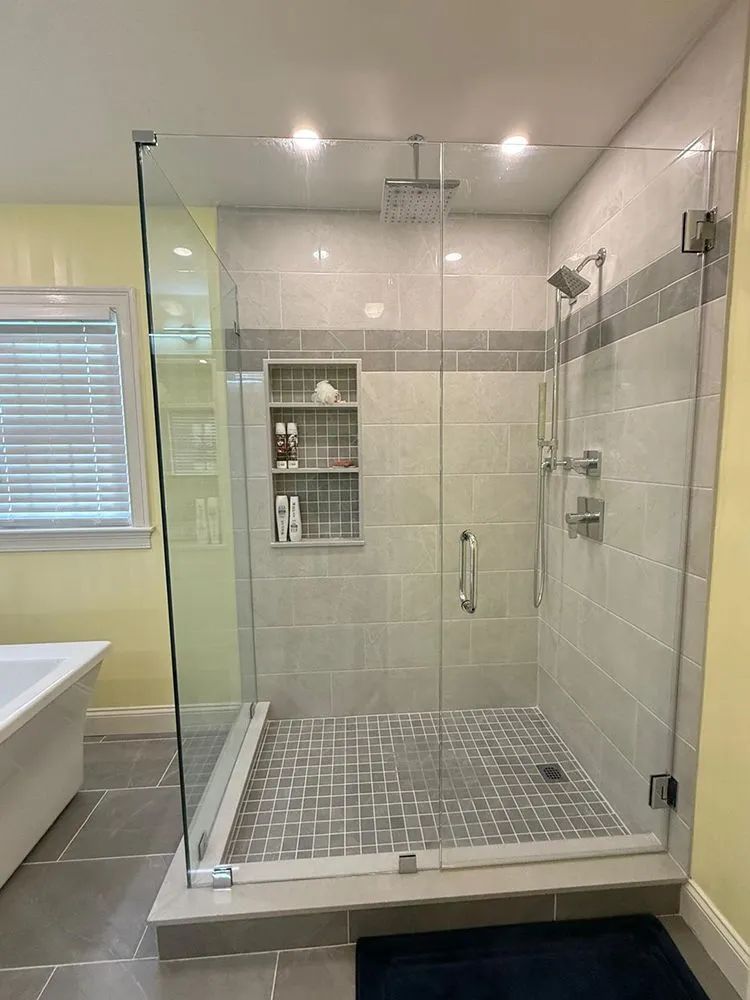 Modern walk-in shower with glass doors, gray tiles, and built-in shelf.