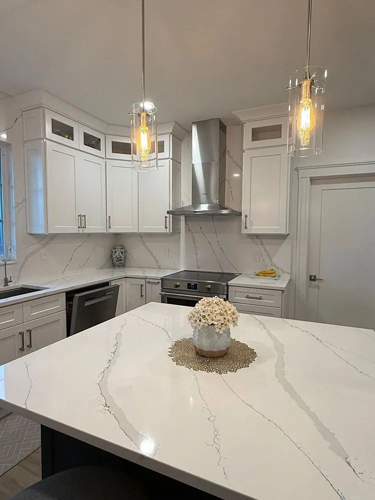 Modern white kitchen with island, quartz countertops, stainless steel appliances, and pendant lights.