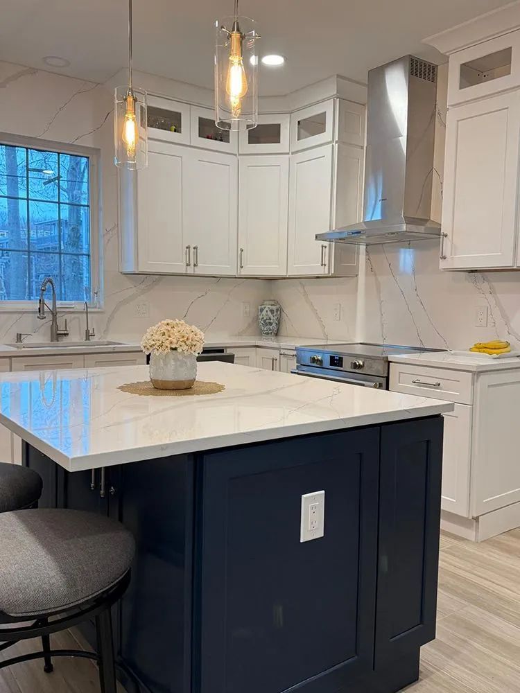 Modern kitchen with white cabinets, navy island, marble countertops, and pendant lights.