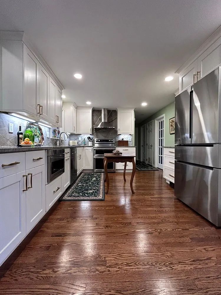 White kitchen with wooden floors, stainless steel appliances, and overhead lighting.