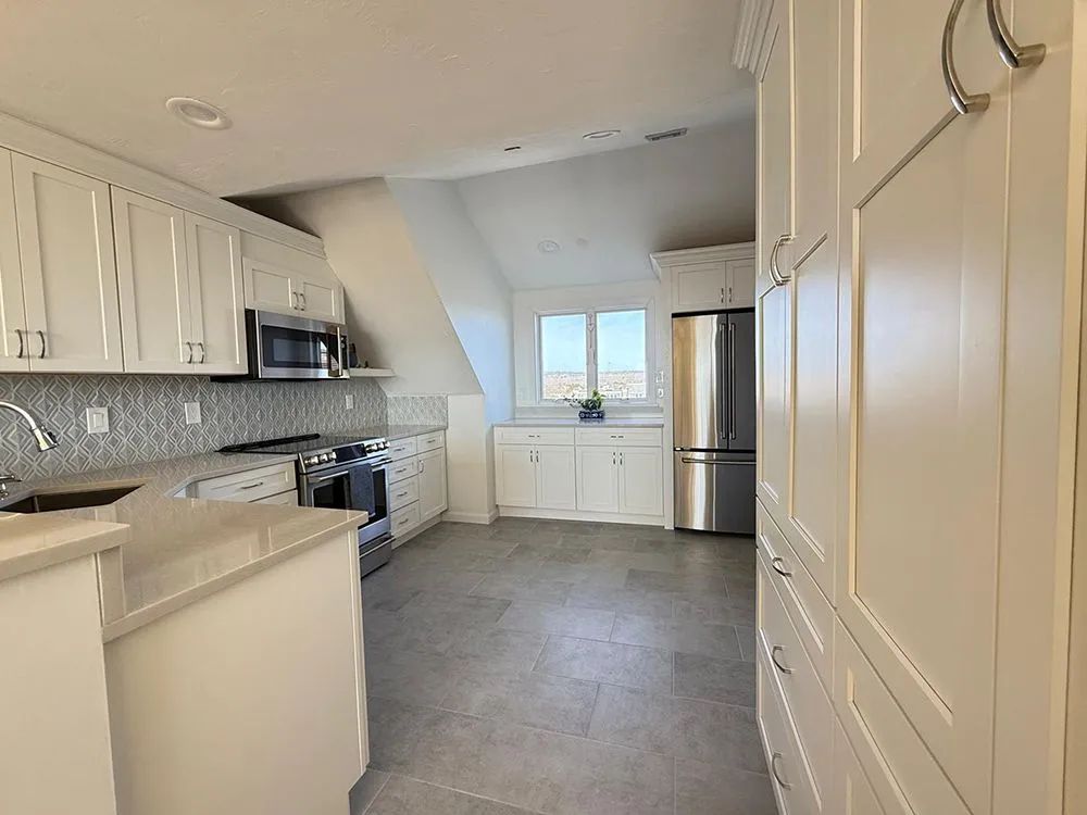 White kitchen with stainless steel appliances, cabinets, and a window.