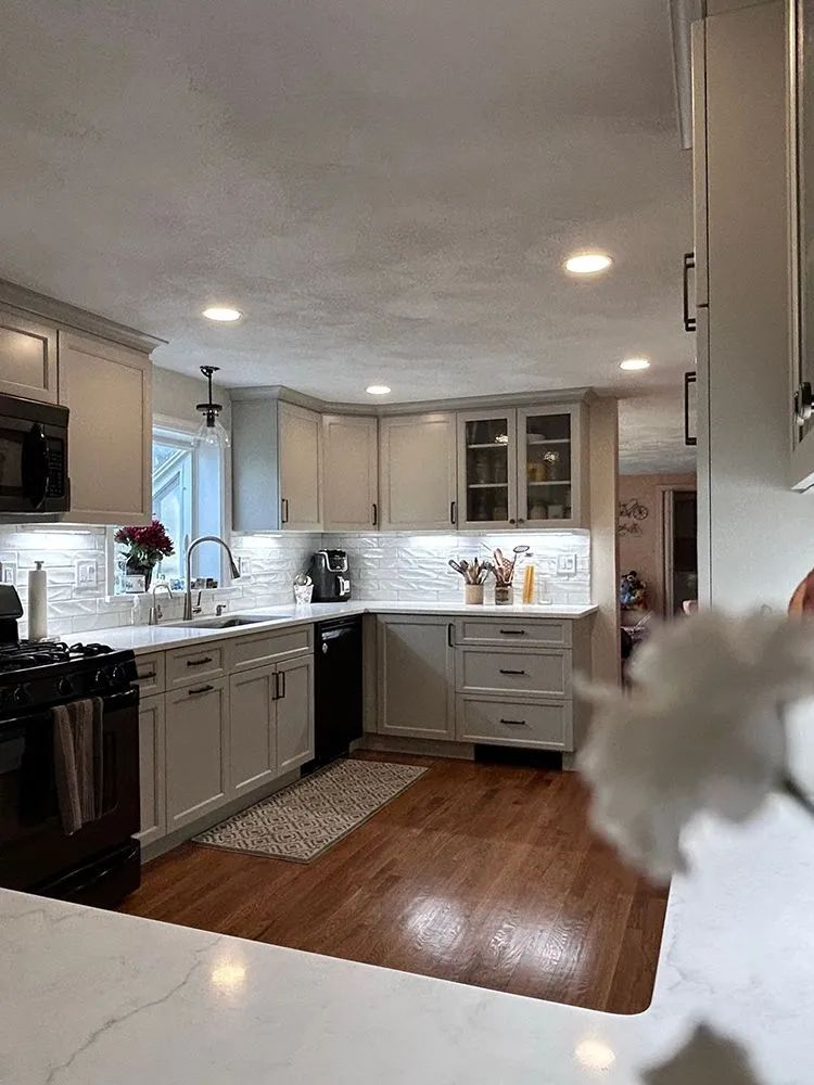 Modern kitchen with light gray cabinets, white countertops, black appliances, and wooden floors.