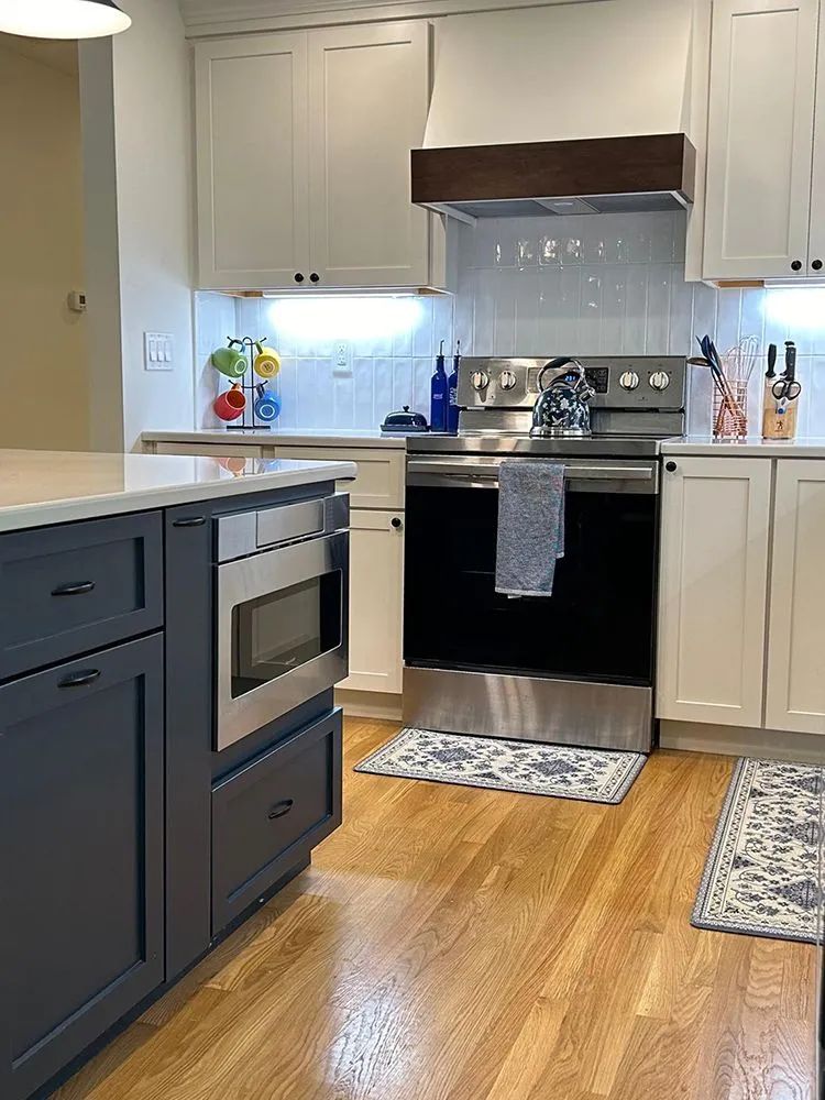 Kitchen with white and blue cabinets, stainless steel appliances, and wooden floor.