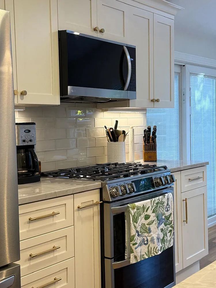 White kitchen with stainless steel appliances, stove, microwave, cabinets, and light backsplash.