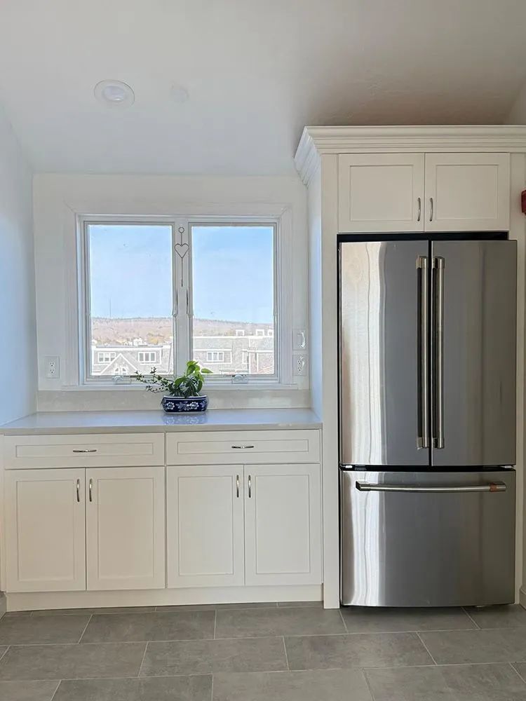 White kitchen cabinets and refrigerator with a window view.