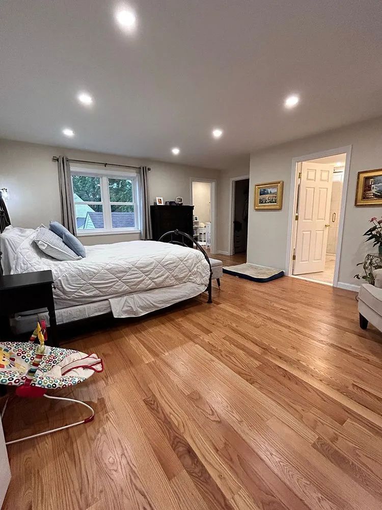 Bedroom with hardwood floors, bed, dresser, doorway, and overhead lighting.
