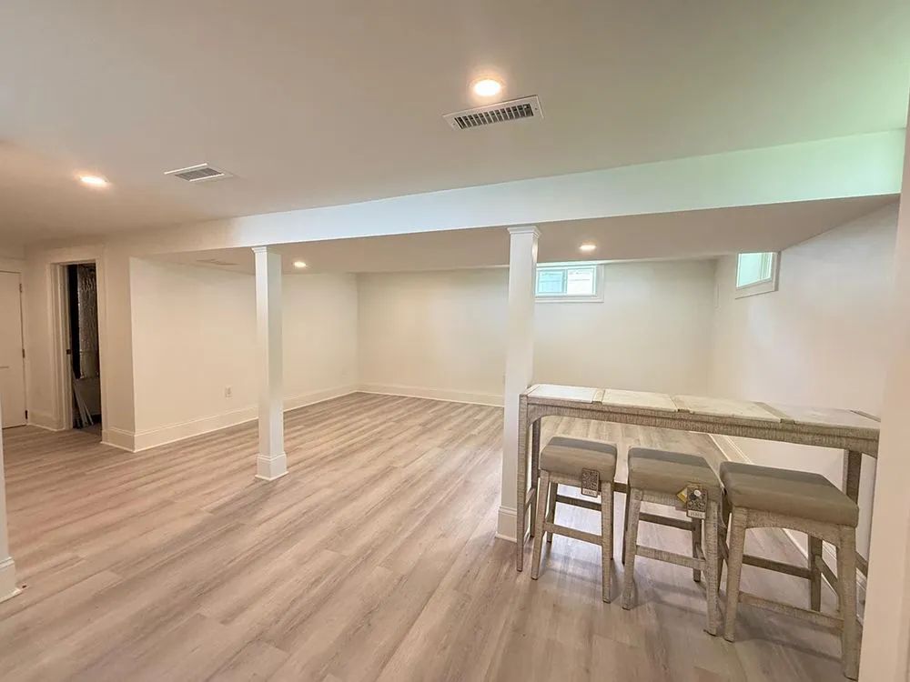 Empty, bright room with gray flooring. Bar with stools in the foreground, white walls, and recessed lighting.