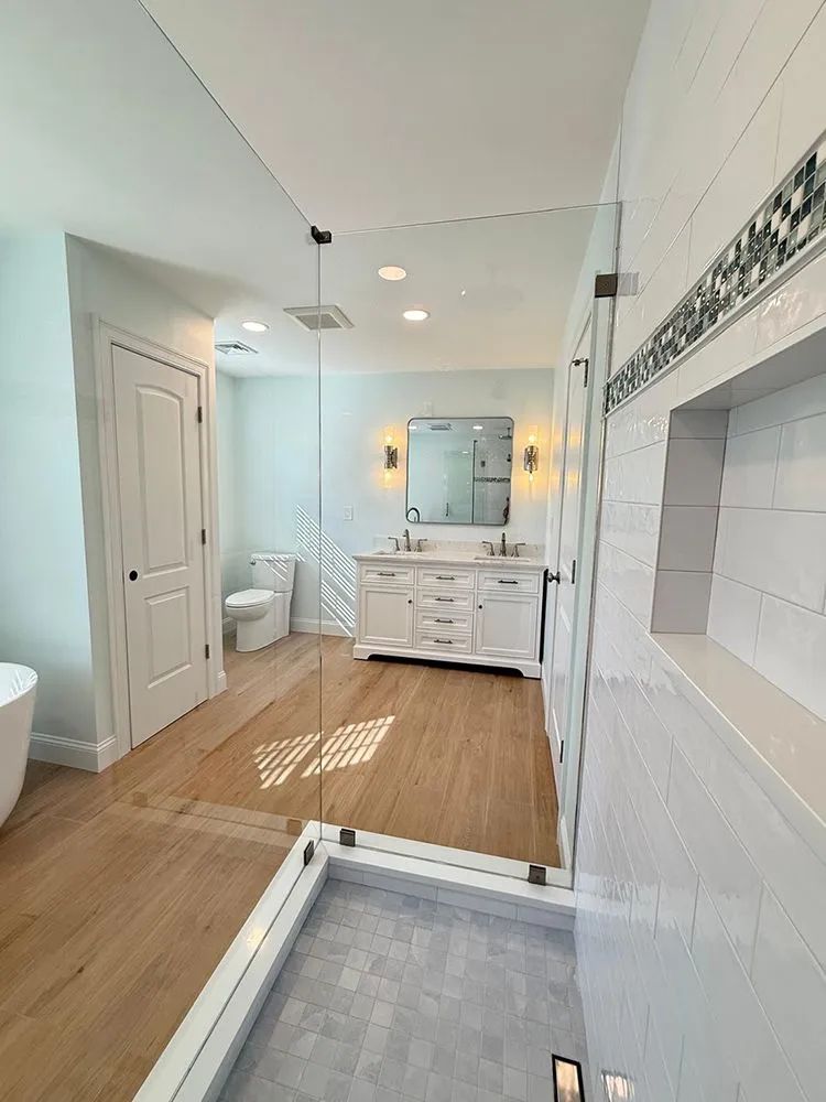Bathroom with a glass shower, double vanity, toilet, and light wood floors.