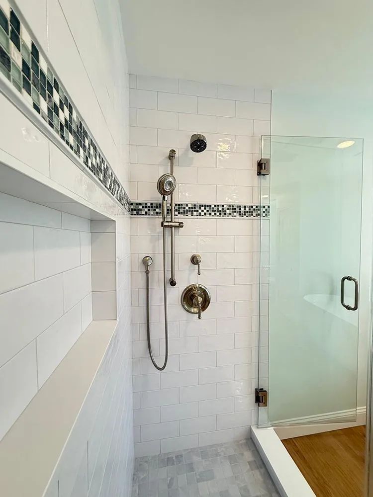 White tiled shower with glass door and decorative tile border; faucet fixtures.