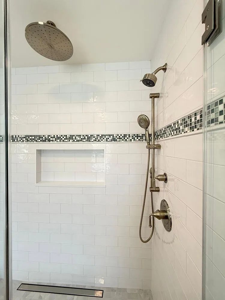 Modern white tiled shower with two shower heads, a built-in shelf, and a decorative tile border.