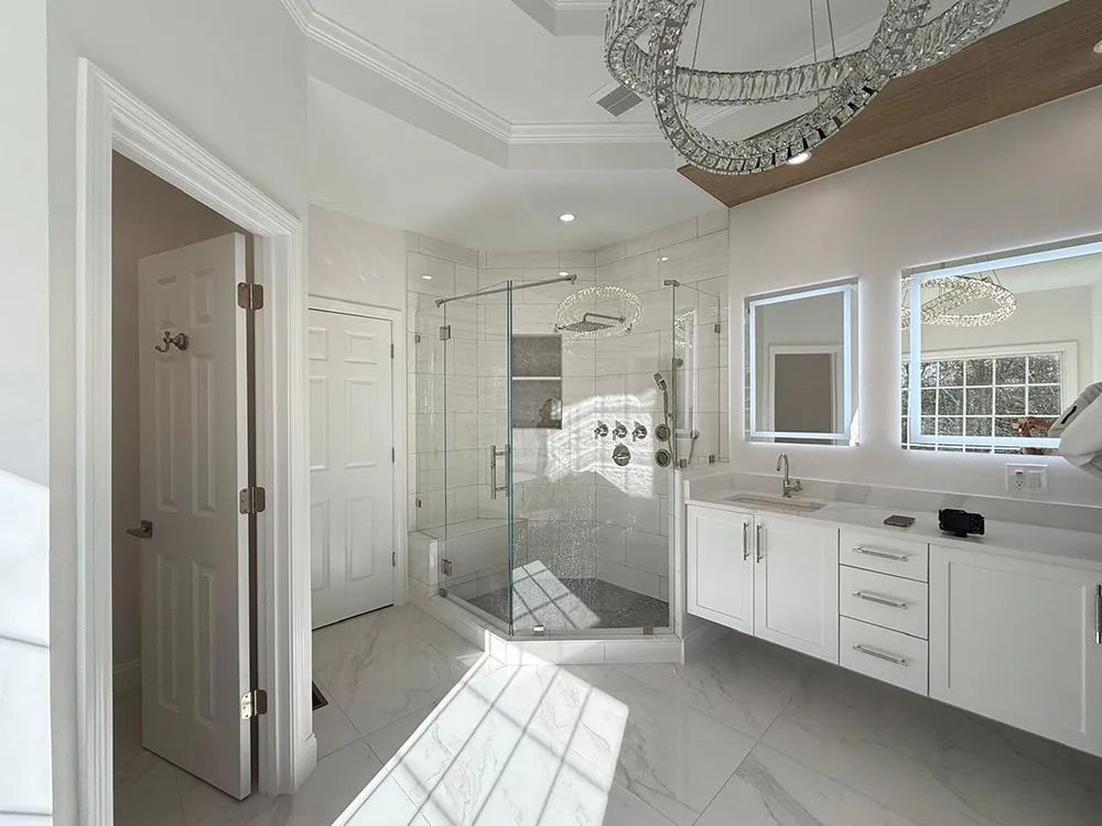 Bright white bathroom with a glass shower, double vanity, and a chandelier.