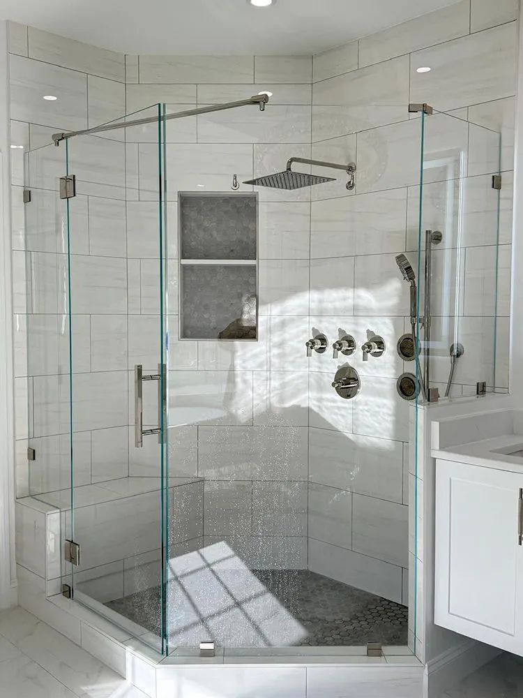 Modern glass shower with white tile walls, a stone floor, and silver fixtures.
