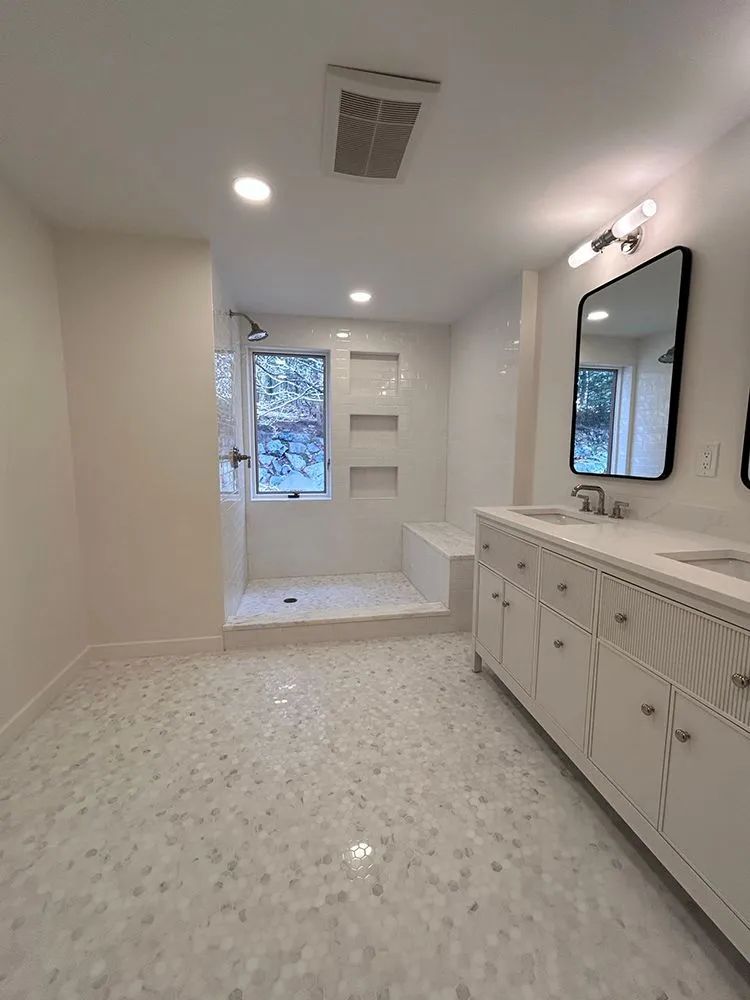 Bright white bathroom with a tiled shower, double vanity, and mosaic floor.