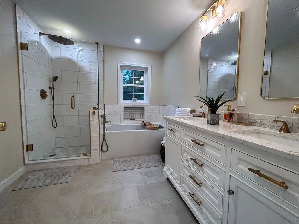 Bathroom with white cabinets, gold fixtures, marble countertop, glass shower, and a soaking tub.