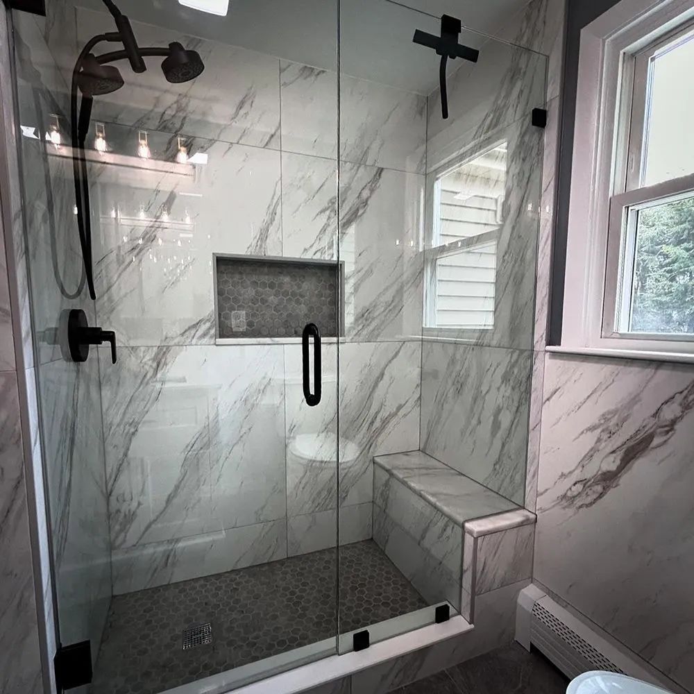 Modern shower with marble-look tiles, glass enclosure, black fixtures, built-in bench, and small window.