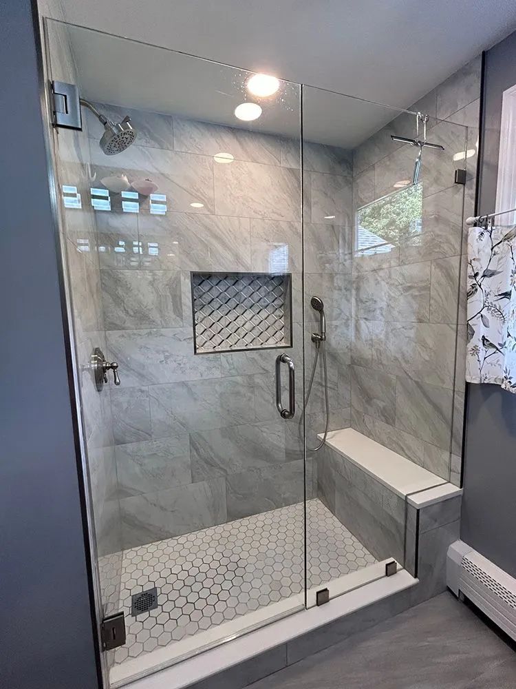 Glass-enclosed shower with gray tiled walls and floor, built-in bench, and a niche for toiletries.
