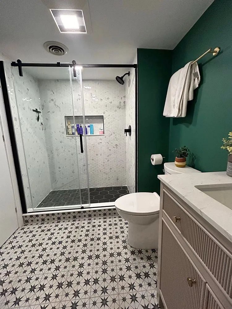 Modern bathroom with patterned floor tiles, green accent wall, glass shower, and vanity.
