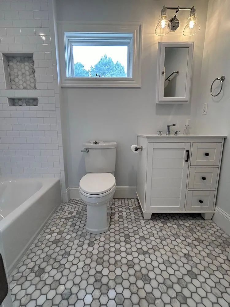 Bathroom with white fixtures, subway tile, and hexagon floor tiles. Features a window, vanity, and toilet.