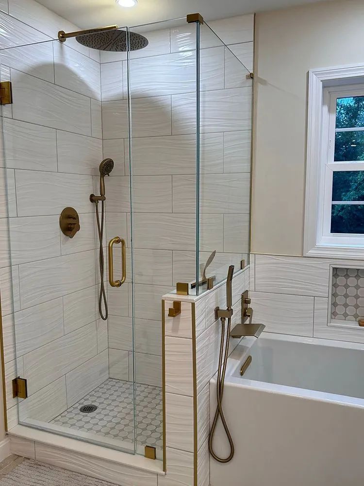 Modern bathroom with white textured tile and glass shower enclosure, gold fixtures.