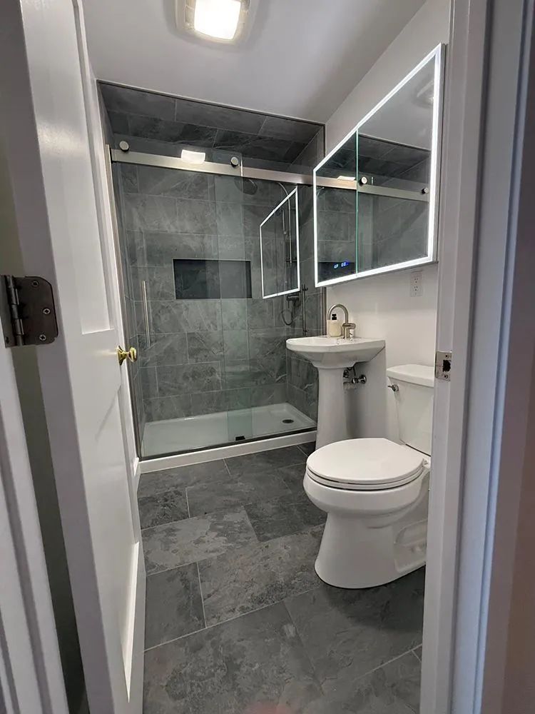 Small modern bathroom with gray tile shower and floor, white toilet and sink.