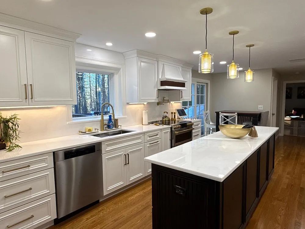 White kitchen with dark island, stainless steel appliances, and gold pendant lights.