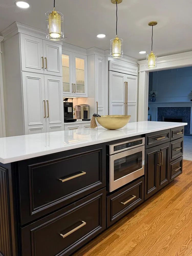 Kitchen with black island, white cabinets, gold pendant lights, and stainless steel microwave.