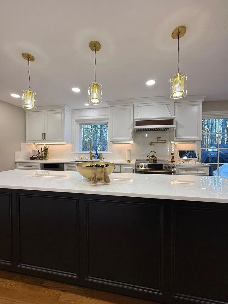 Modern kitchen with black island, white countertops, and three gold pendant lights.