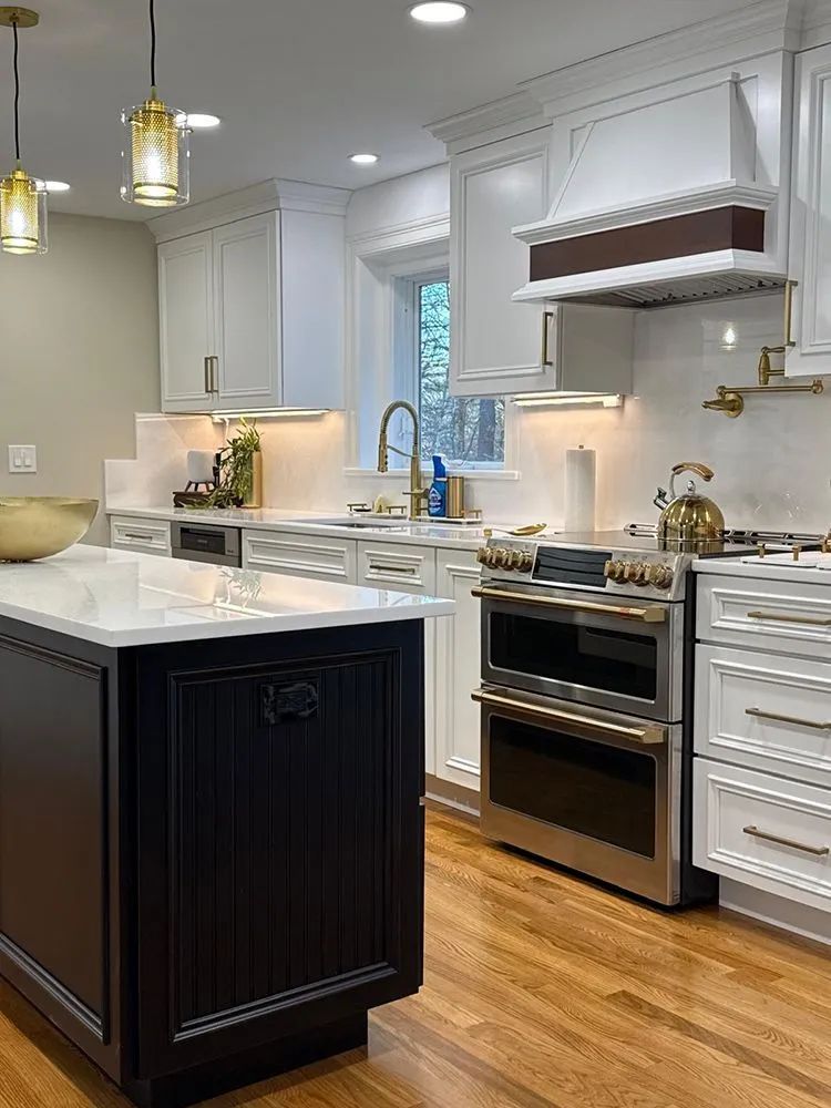 Elegant white kitchen with black island, gold accents, stainless steel oven, and wooden floor.