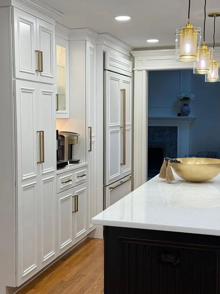 White kitchen with gold hardware, coffee station, and black island with a gold bowl.