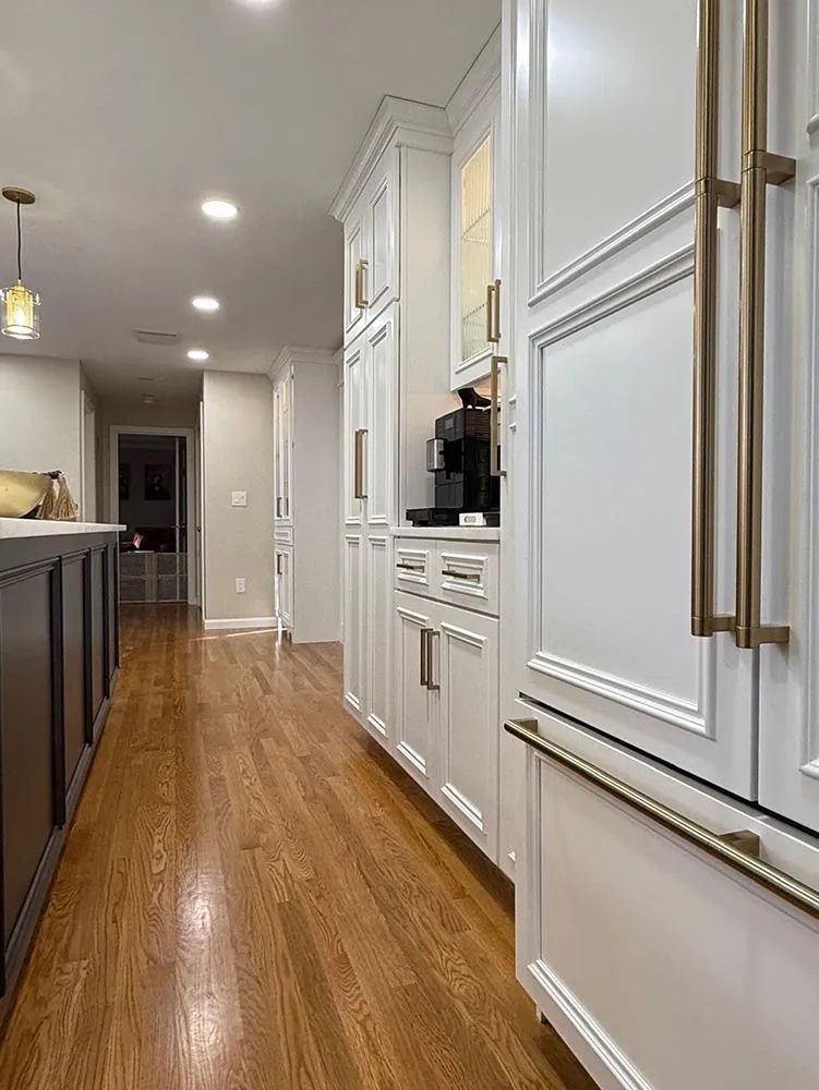 White kitchen cabinets with gold hardware and a built-in coffee machine, wood floor.