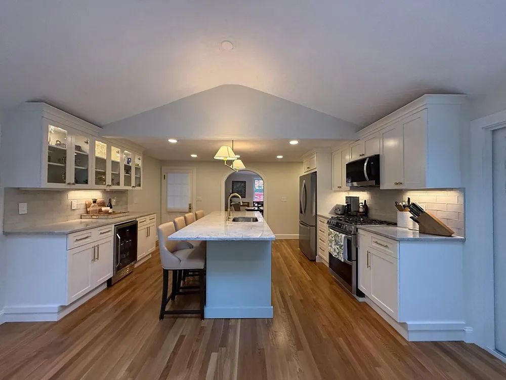 Bright white kitchen with a large island, stainless steel appliances, and wooden floors.