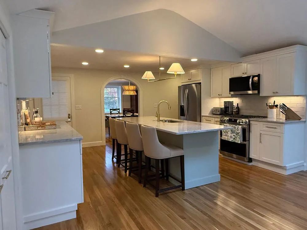 Modern white kitchen with island, hardwood floors, stainless steel appliances, and beige walls.