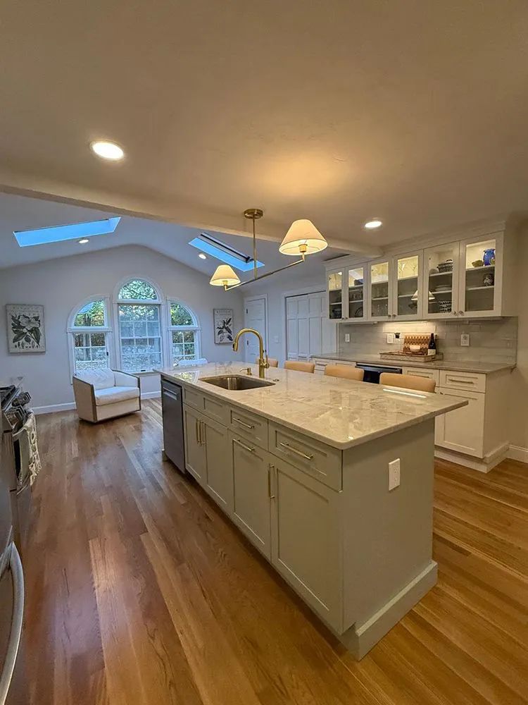 Spacious kitchen with island, white cabinets, and wooden floors. Natural light streams in from arched window.