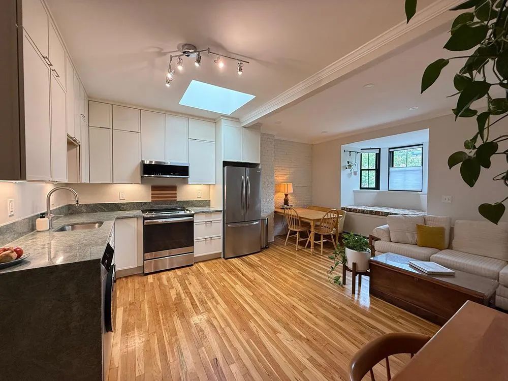 Kitchen with wooden floors, white cabinets, stainless steel appliances, and a small dining area.