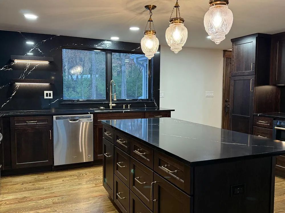 Kitchen with dark cabinetry, black countertops, stainless steel appliances, island, pendant lights.