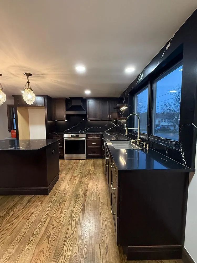 Dark wood kitchen with granite countertops, stainless steel appliances, and large windows.