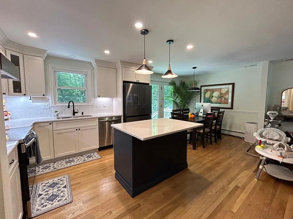 Kitchen with white cabinets, dark island, stainless steel appliances, and wood floors. Dining area visible.