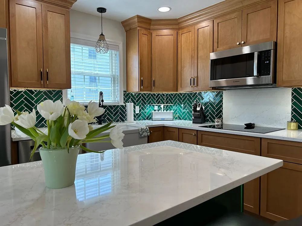 Kitchen with light wood cabinets, white countertops, green tile backsplash, and a vase of white tulips.
