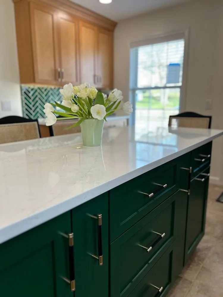 Green kitchen island with white countertop and a vase of white flowers.