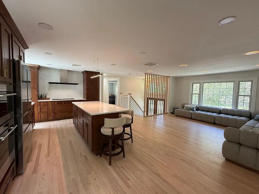 Open-concept kitchen with island, wooden cabinets, and a seating area with a large sofa and light-colored hardwood floors.