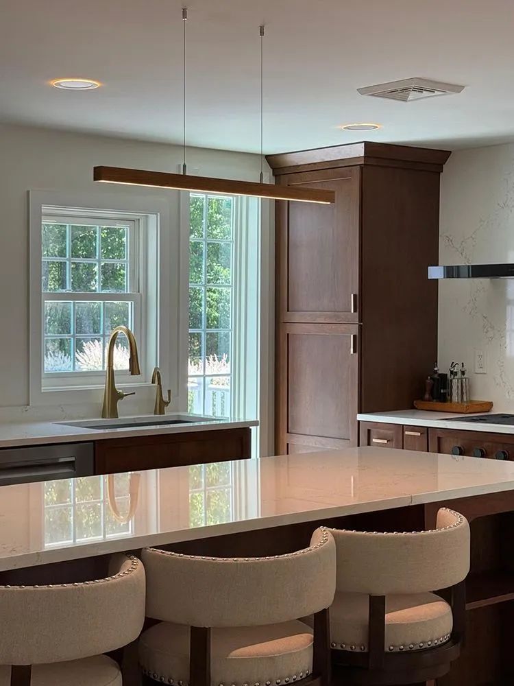 Kitchen with white island, dark cabinets, gold fixtures, and a long, linear pendant light.