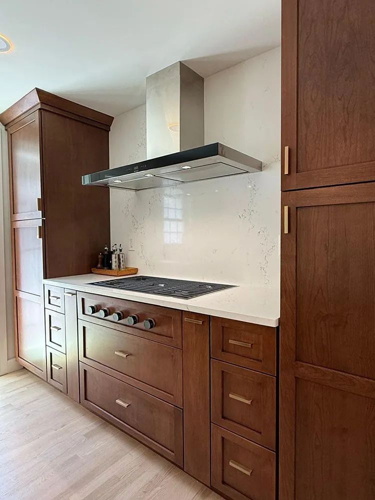 Kitchen with brown cabinets, white countertop, stainless steel hood, and cooktop.