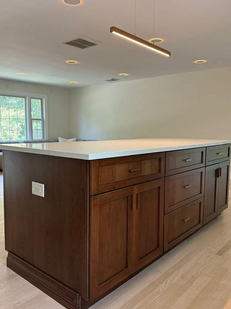Kitchen island with brown cabinets, white countertop, recessed and linear lighting.