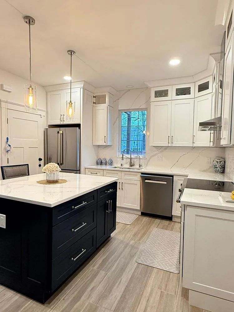 Modern kitchen with navy island, white cabinets, stainless steel appliances, and wood-look flooring.
